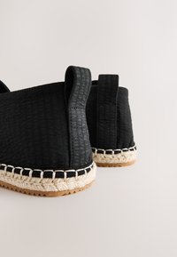 Black espadrille shoes with a textured fabric upper, stitched jute sole, and a contrasting white rope accent along the edge.