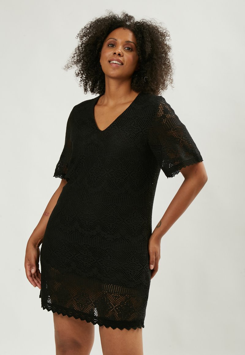 Schwarzes gehäkeltes Kleid mit V-Ausschnitt, kurzen Ärmeln und gewelltem Saum. Verfügt über ein kompliziertes Spitzenmuster und eine figurbetonte Silhouette.