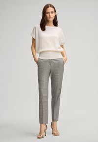 Helle beige, lässig geschnittene Pullover mit geripptem Saum, kombiniert mit grauen Karomuster-Anzughosen und goldenen Absatzsandalen.