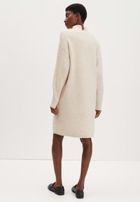 Strickkleid in Cremeweiß, mit hohem Kragen und langen Ärmeln. Weicher Stoff mit gerader Silhouette, das bis zur Mitte des Oberschenkels reicht.