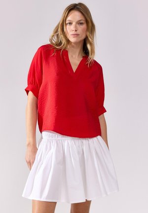Röd, texturerad kortärmad topp med V-ringning, tillsammans med en vit, rynkad knä-length kjol. Kontrast mellan djärva färger och material.