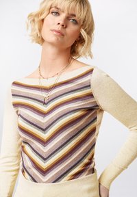 Strickoberteil mit einem Zickzackmuster, das Streifen in Senfgelb, Lila und Schwarz zeigt. Helle gelbe strukturierte Ärmel und ein weiter Ausschnitt.