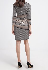 Black and beige patterned dress featuring a fitted design, three-quarter sleeves, and a knee-length hem. Elevated with high-heeled shoes.