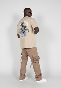 Beige graphic t-shirt features a black and blue printed design on the back. Paired with khaki cargo pants and white sneakers.