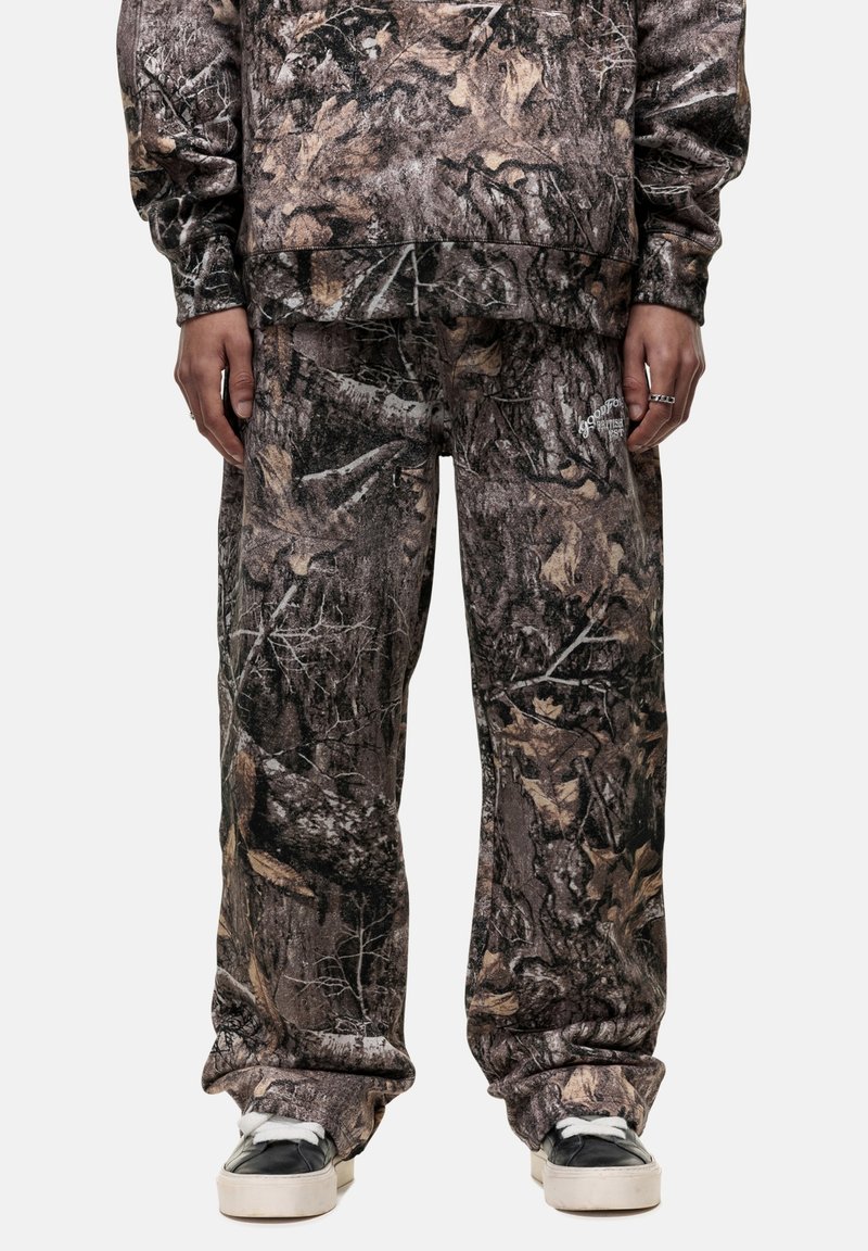 Camo-print sweatshirt and pants in brown, black, and earthy tones, featuring a relaxed fit and soft texture. Black footwear with white accents.