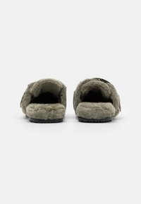 Grå fluffiga tofflor med öppen baksida, mjukt innerskal, hållbar texturerad sula och justerbar rem för enkel användning.