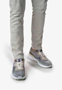 Zapatillas grises con una mezcla de materiales de ante y malla, con cordones blancos, un diseño estratificado y una suela texturizada.