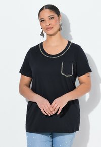 Camiseta negra de manga corta con escote redondo, adornada con tachuelas plateadas en el escote y el bolsillo. Material de algodón suave.