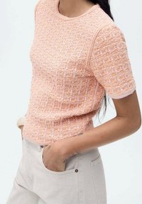 Haut en maille texturée à manches courtes de couleur orange clair avec des accents roses. Encolure ronde, coupe près du corps, avec des motifs brodés complexes.