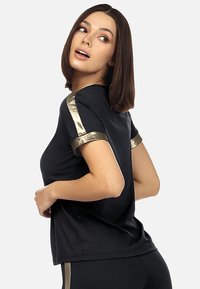 Czarna sportowa koszulka z metalicznymi złotymi akcentami na rękawach. Posiada luźny krój i gładką teksturę materiału, zaprojektowana z myślą o komforcie.