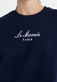Felpa blu navy realizzata in tessuto morbido, con ricamo "Le Marais" e "PARIGI" in testo bianco a contrasto sul petto. Collo rotondo.