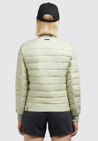 Light green puffer jacket with quilted design, ribbed cuffs, and a smooth texture. Worn with black denim shorts and a black cap.