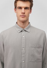 Gray long-sleeve shirt made of textured fabric, featuring a buttoned front, collared neckline, and a left chest pocket.