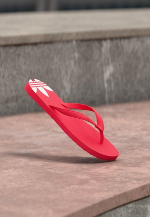 Chancla roja con diseño de logo blanco, colocada en ángulo sobre escalones de piedra al aire libre.