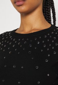 Pull noir avec un col rond et des ornements de clous ronds et transparents dispersés sur le devant, présentant un design texturé.