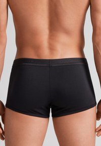 Černé boxerky vyrobené z hladkého materiálu, s elastickým pasem a brandovaným textem. Design je přiléhavý a bezproblémový na okrajích.