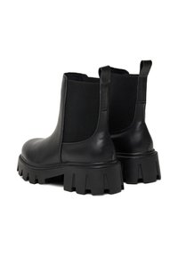 Mustad mustad nahast Chelsea saapad paksude tõsteaedade ja elastsete külgpanelidega, nähtud tagant.