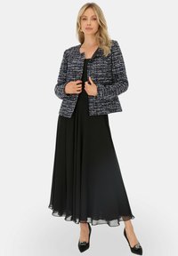 Marynarsko-niebieska i biała kurtka z tweedu o dopasowanym kroju, zestawiona z luźną czarną sukienką. Czarne szpilki dopełniają całość.