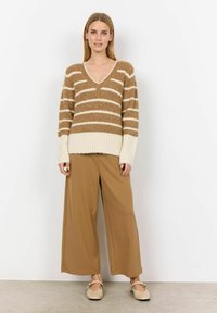 Brown en crèmekleurige gestreepte trui met een V-hals, gecombineerd met brede bruine broeken en beige flats, wat een gelaagde, casual look creëert.