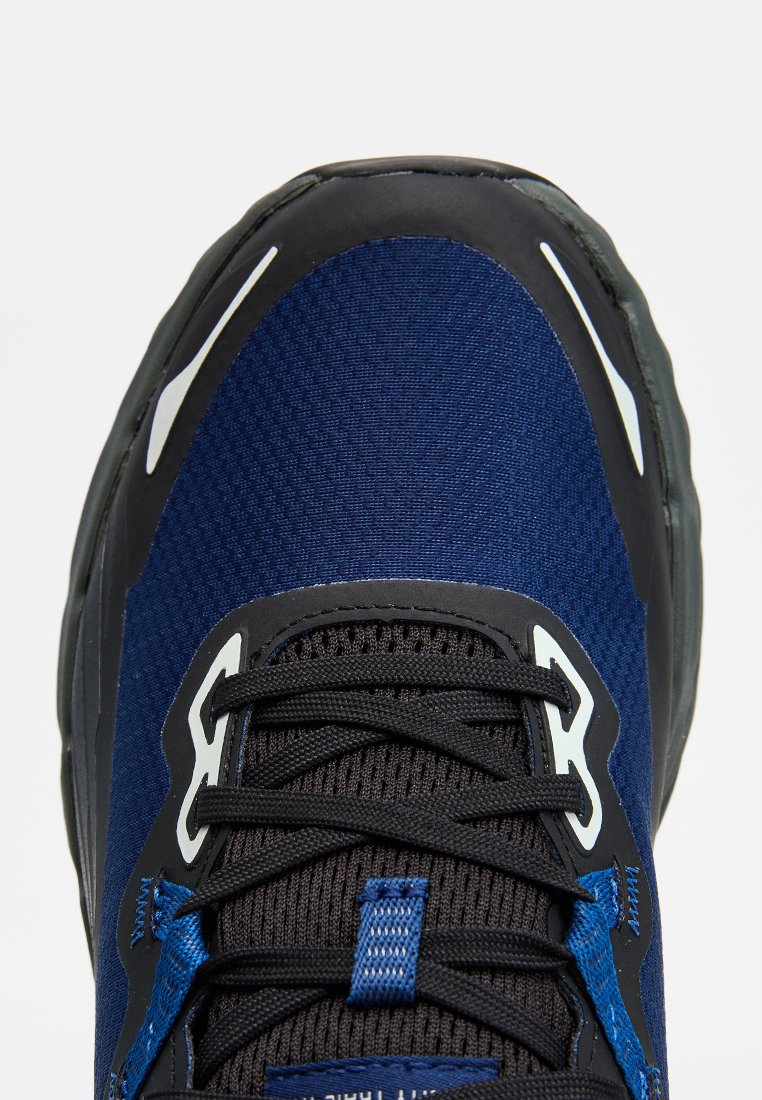 Gros plan sur une chaussure de sport bleu marine et noire avec des lacets noirs et des détails réfléchissants blancs sur l'avant et les côtés.