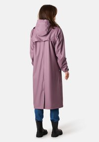 Lange, paarse regenjas van waterdicht materiaal, met een capuchon, zijsplitten en lange mouwen, gecombineerd met donkere rubberen laarzen.