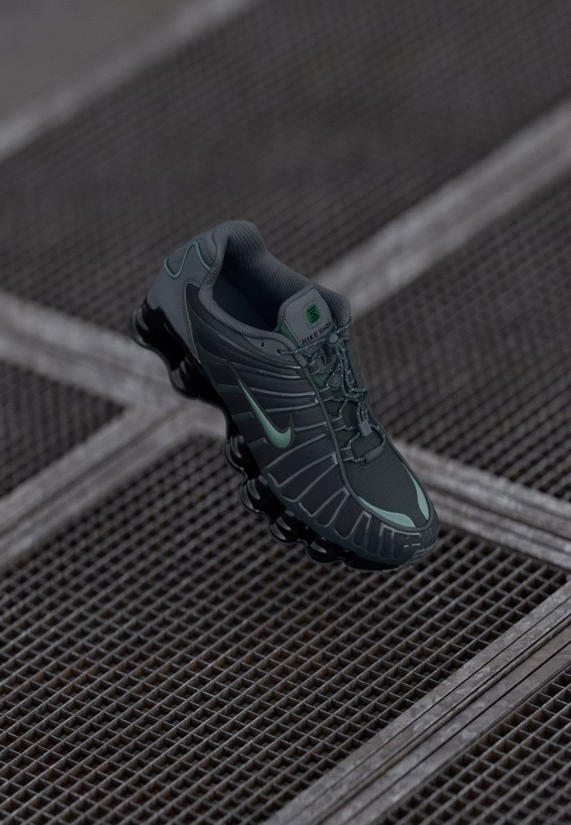 Tamnozeleni Nike tenisice za trčanje s crnim segmentiranim đonom suspendirane iznad metalne mrežne podloge s isprepletenim linijama.