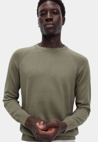 Maglione a maglia verde oliva con scollo rotondo e polsini a coste, caratterizzato da una texture liscia e un design a maniche raglan.