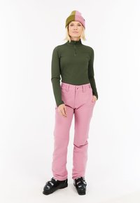 Groene lange mouw top met een rits hals, gecombineerd met lichtroze skibroeken en zwarte skischoenen. De beanie heeft roze en groene strepen.