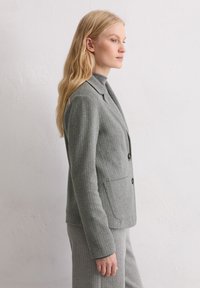 Blazer gris clair à fines rayures avec une coupe ajustée, un design à simple boutonnage et trois boutons. Il dispose de deux poches latérales et d'une texture lisse.