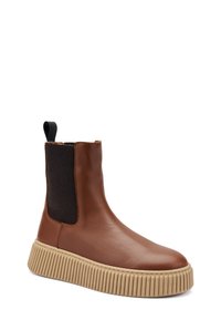 Botín de cuero marrón hasta el tobillo con panel lateral elástico, acentos de tela negra y suela acanalada color beige. Textura suave y tira en la parte trasera.