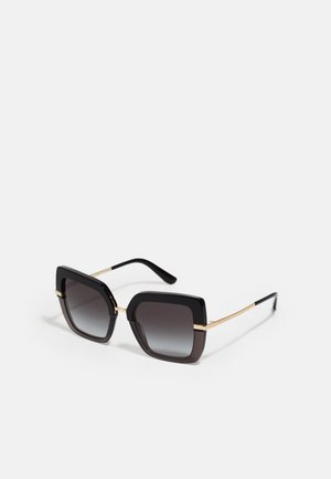 Gafas de sol negras en forma de cuadrado con lentes gris degradado. Acentos dorados en la montura, con un acabado mate suave. Las patillas son delgadas y brillantes.
