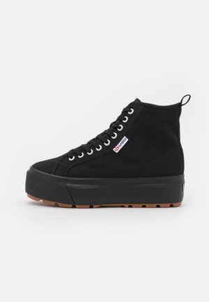 Czarny wysokiej klasy sneaker z płóciennego materiału z grubą podeszwą na platformie, białe oczka, czarne sznurowadła i mała prostokątna metka z logo po boku.