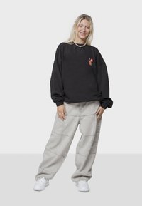 Sudadera negra de gran tamaño con un gráfico pequeño; pantalones grises claros, holgados, con detalles en las costuras; zapatillas blancas; textura suave.