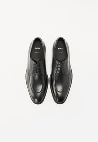 Scarpe da uomo in pelle nera caratterizzate da una superficie liscia, punta arrotondata, design con lacci a cinque occhielli e dettagli di cucitura discreti.