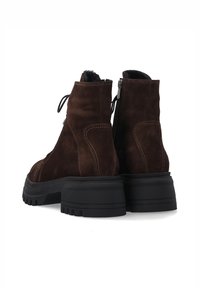 Bruine suède enkellaarzen met een stevige zwarte rubberen zool, voorzien van een zijrits en vetersluiting, met zichtbare stiknaden als detail.