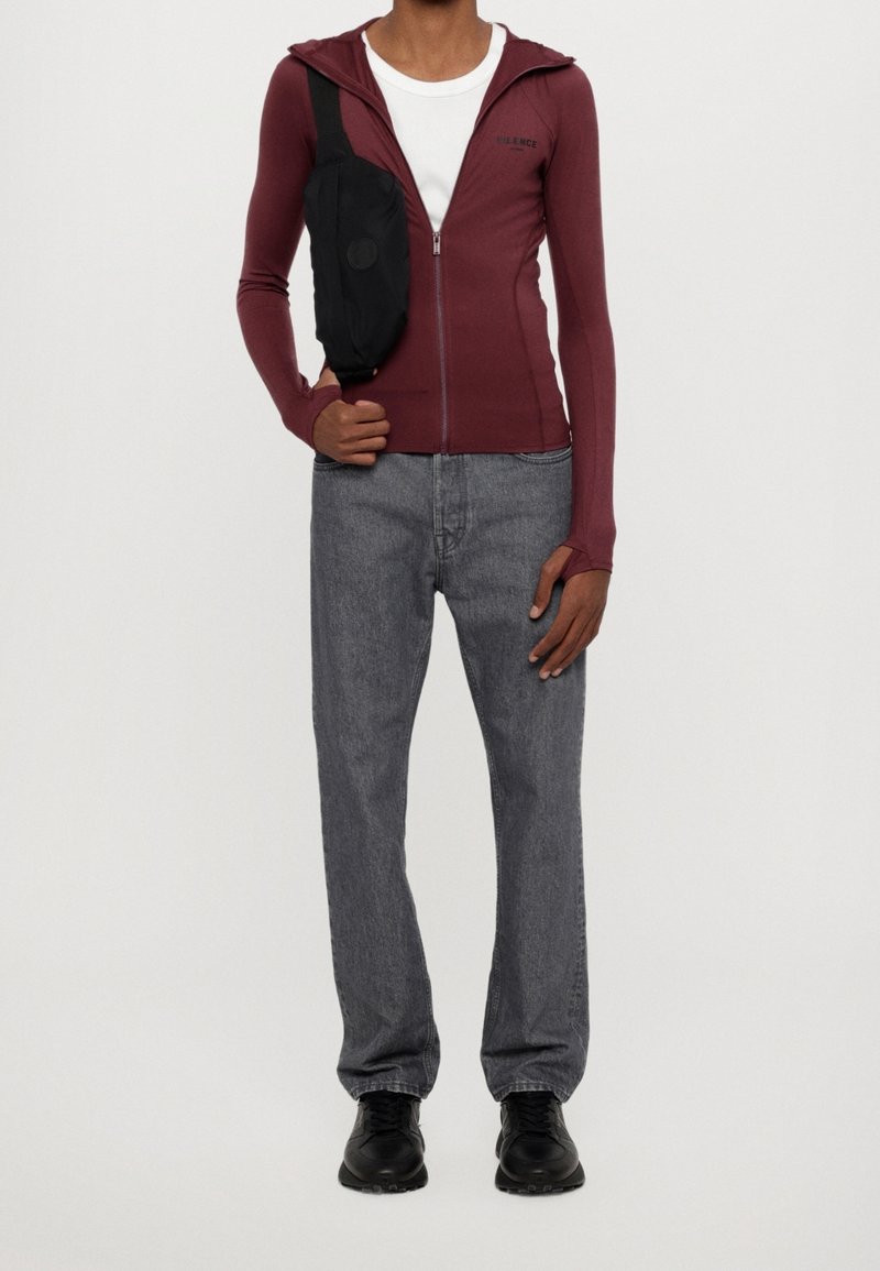 Vínová mikina na zip s žebrovanou texturou, zkombinovaná se šedými džíny a černými teniskami. Na rameni je nošená černá kabelka přes tělo.