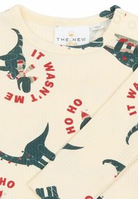 Krem košulja s dugim rukavima koja sadrži print dinosaura s blagdanskim elementima i crveni tekst "NISAM JA" s rebrastom teksturom i zatvaranjem na snap.