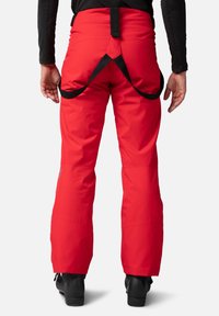 Röda skidbyxor med lös passform, justerbara svarta remmar i midjan, förstärkta muddar och en smidig textur. Lämpliga för vintersporter.