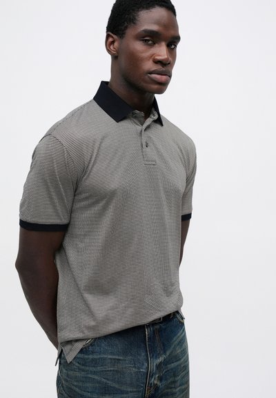 Trumpos rankovės polo marškiniai juodai-baltame languotame rašte su tamsiai mėlynu apykakle. Medvilnės audinys su tekstūruotu paviršiumi. Priekiniai mygtukai kaip detalė.