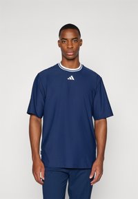 Tamsiai mėlynas trumpomis rankovėmis marškinėliai su apvaliu kaklu, turintys baltą ripsinį apykaklę ir mažą Adidas logotipą ant krūtinės.