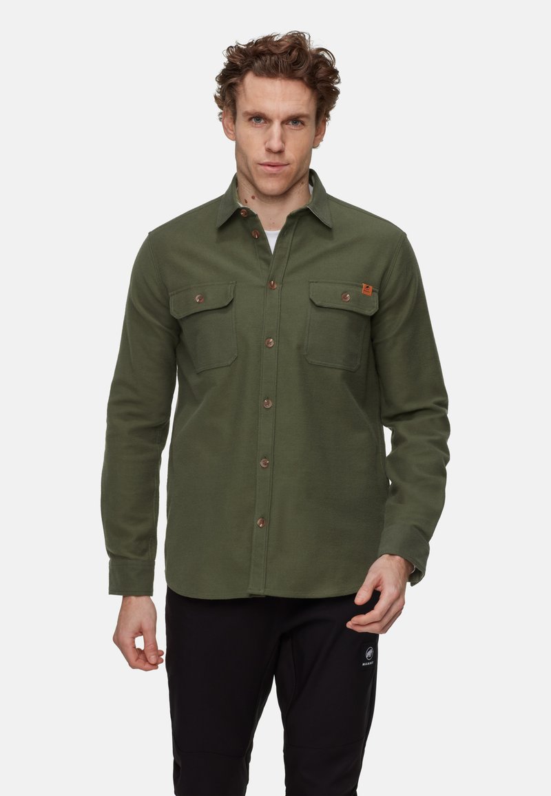 Olivgrön flanellskjorta med lång ärm, två bröstfickor och bruna knappar. Materialet verkar mjukt med en texturerad finish.