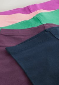 Pile de t-shirts en coton pliés en violet, bleu marine, vert, rose et magenta, montrant le col et les coutures des épaules.