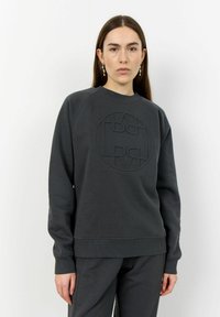 Sweatshirt gris avec un logo circulaire texturé à l'avant, doté d'un col rond et de poignets côtelés, associé à un pantalon assorti.