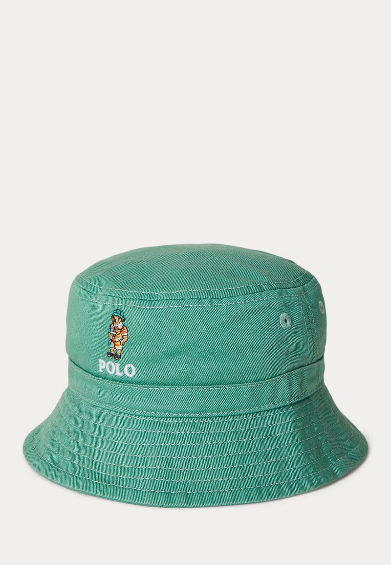 Žalias medvilninis kibiro skrybėlė su siūtomis siūlėmis, išsiuvinėtu Polo logotipu ir personažo detale šone. Įrengti du ventiliacijos angos.