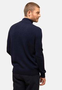 Ciemnogranatowy sweter z wysokim kołnierzem, o dzianinowej fakturze i dopasowanych rękawach. Gładki design z szerokim dołem, noszony na eleganckich spodniach.