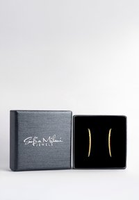 Guldtonade örhängen i en svart sammetsfodrad presentask med en texturerad grå utsida, som har en minimalistisk böjd design.