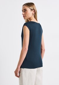 T-shirt aderente blu navy con maniche corte e scollatura arrotondata, realizzata in tessuto morbido. Indossata con pantaloni larghi di colore chiaro.