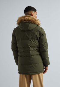 Oliwkowa kurtka puchowa z kapturem wykończonym futrem, z pikowanym wzorem i bocznymi kieszeniami, pokazana z tyłu. Gładka faktura.
