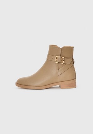 Bottes ankle beiges en cuir lisse, avec un bout rond, une sangle à boucle sur le côté et un petit talon empilé. Design simple et moderne.