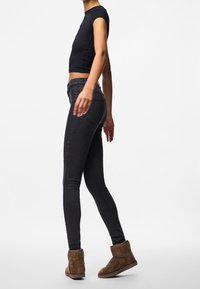 Úzké džíny v tmavém denimu, kombinované s přiléhavým černým tričkem a hnědými semišovými kotníkovými botami. Oblečení vykresluje elegantní, moderní siluetu.